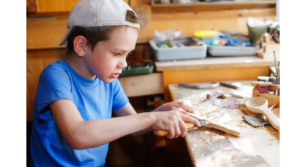 A boy is wood carving with a knife.