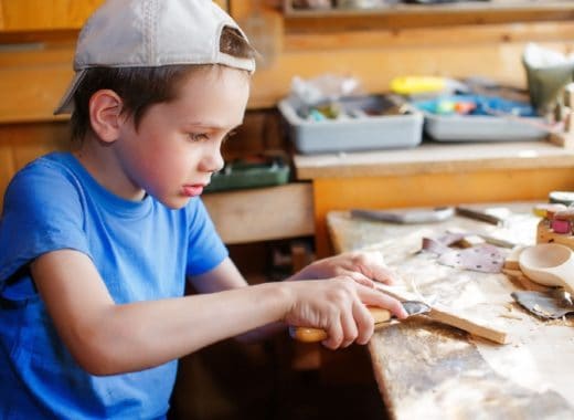 A boy is wood carving with a knife.
