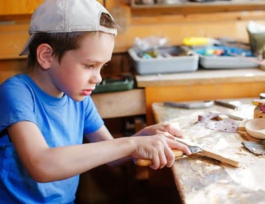 A boy is wood carving with a knife.