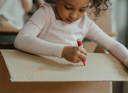 A girl colors on a cardboard box.