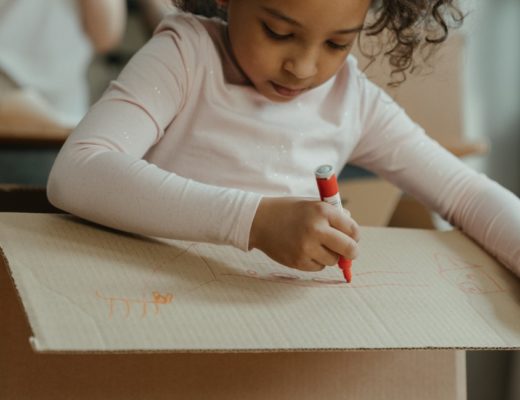 A girl colors on a cardboard box.