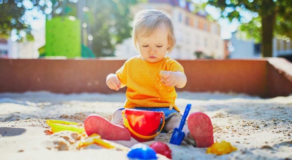 a one year old plays with outdoor toys in the sand